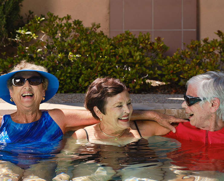 Three senior woman laugh while sitting in a hot tub together