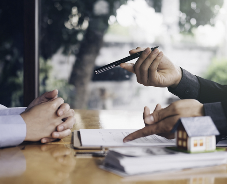 Photo focused on hands of people sitting across from each other at a desk reviewing home ownership paperwork
