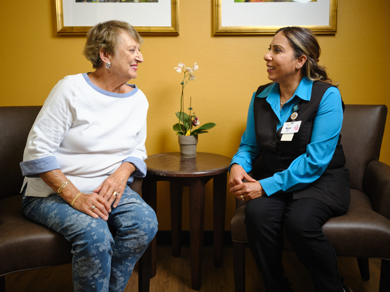A senior woman and a health care professional sit and talk with each other